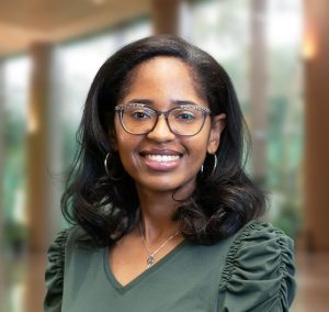 Skye is wearing glasses, a necklace with a key charm, and a green shirt with ruffled sleeves.
